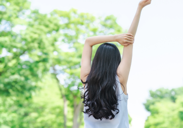 木々の前で伸びをしている女性の後ろ姿の写真