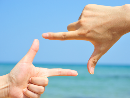 海に向かって指でカメラを作っている写真